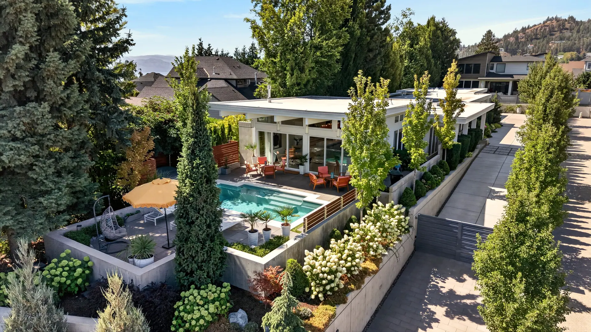 Aerial drone photo of a modern West Kelowna home with a pool and landscaped yard